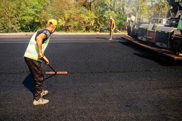 Road construction crew used shovels to scatter more asphalt over the top of the new pavement. At...