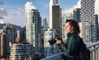 Fototapeta na wymiar Caucasian Woman with camera taking images of modern cityscape. Travel photographer. Cambie Bridge, False Creek, Downtown Vancouver, British Columbia, Canada.