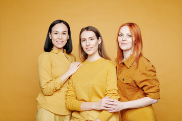 Group of smiling beautiful young multi-ethnic women supporting each other, they standing against yellow background