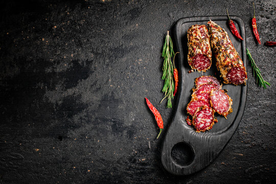 Pieces of salami sausage with dried chili peppers and rosemary. On a black background. High quality photo