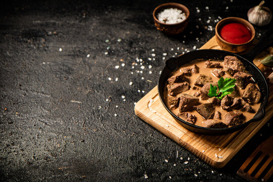 Delicious fried liver in a frying pan with tomato sauce. On a black background. High quality photo