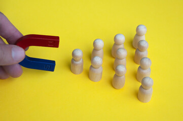 Hand holding magnet attracting wooden dolls on yellow background.