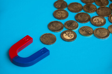 Business concept. Magnet attracting gold coins with blue cover background. Copy space