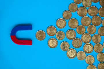 Business concept. Magnet attracting gold coins with blue cover background. Copy space