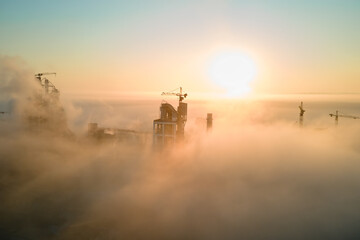 Aerial view of cement factory with high concrete plant structure and tower crane at industrial manufacturing site on foggy evening. Production and global industry concept