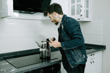 Kitchen, young man using kettle on electric stove, tea making and brewing