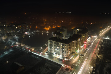 Fototapeta na wymiar Aerial view of high rise apartment buildings and bright illuminated streets in city residential area at night. Dark urban landscape