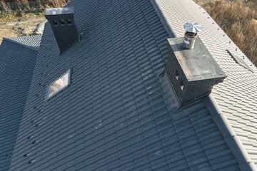 Closeup of attic windows and brick chimneys on house roof top covered with ceramic shingles. Tiled...