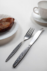 There are a knife and a fork on the table. Nearby is a mug and a plate of steak. On a white background. local focus.