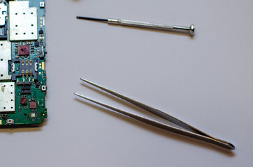 Disassembled mobile phone on the table of a mechanical engineer during repair. Tweezers and screwdriver for repairing electronic gadgets on a white background.