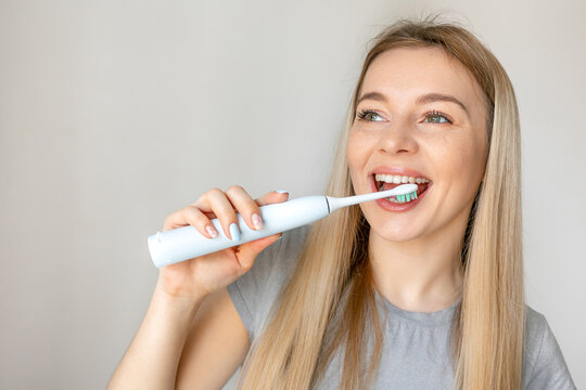 Girl brushing teeth with electric toothbrush. White background.