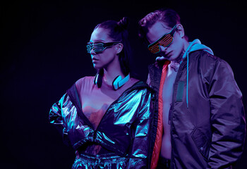 Serious confident modern couple in neon goggles posing against dark background