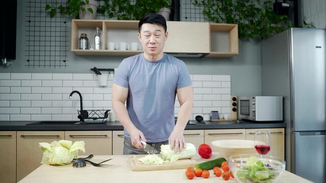 Asian male chef coach tells a recipe how to cook healthy or Chinese food. Looking at the camera. The male records video or online lessons. standing in the kitchen at home. Blogger. Webcam view