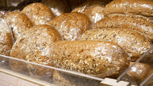 Close-up of many packaged loafs with seeds on a wooden counter and a male hand takes one