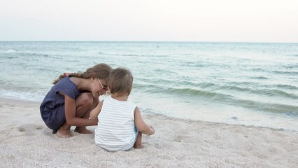 Girl helping her little brother to look for seashells in the sand on the coast