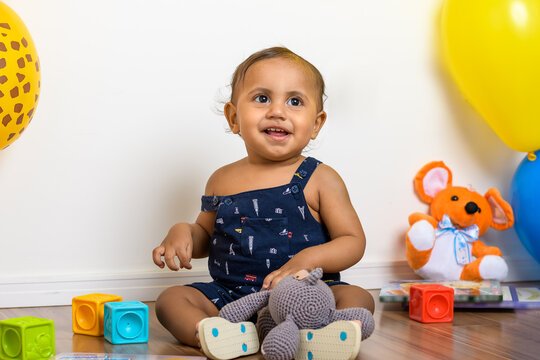 adorable 12 month old baby smiling, sitting among toys, photographed indoors
