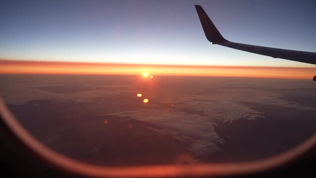 Looking out of window of flying at sunrise airplane. Point of view 4k video footage of amazing scenery during flight. Beautiful sunrise or sunset orange and blue sky outside of passanger air jet
