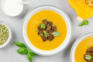 Seasonal autumn roasted pumpkin and carrot soup with cream and rye bread croutons on a light concrete background. Top view.