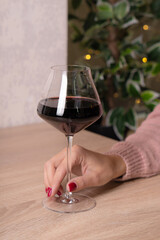A glass of red wine on a beige light wooden table in a restaurant. The girl is holding a glass.