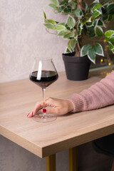A glass of red wine on a beige light wooden table in a restaurant. The girl is holding a glass.