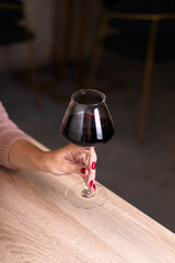 A glass of red wine on a beige light wooden table in a restaurant. The girl is holding a glass.