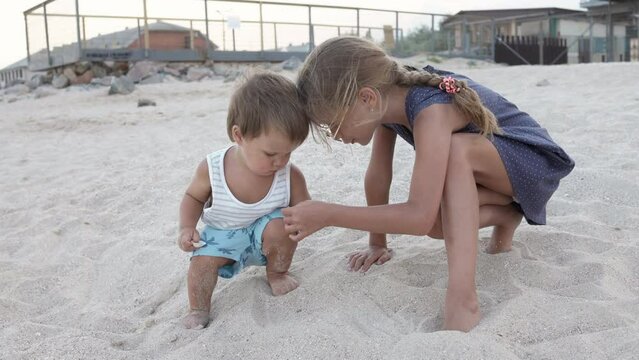 Girl helping her little brother to look for seashells in the sand on the coast