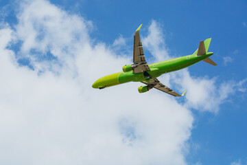 Passenger plane of yellow-green color flies in the blue sky with white clouds,, air transportation concept, population evacuation