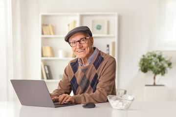 Smiling elderly man sitting at home and using a laptop