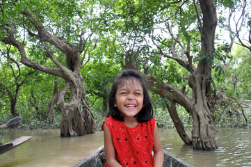 Cute little girl rejoices vacation at Ratargul swamp forest during a ride on a boat. She was luxuriating in a delightful vacation trip. Wearing a red tunic dress and closed eyes.