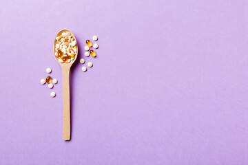 Vitamin capsules in a wooden spoon on a colored background. Pills served as a healthy meal. Drugs, pharmacy, medicine or medical healthycare concept
