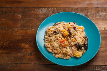 A large dish of couscous with saffron and nuts on a wooden table. save a place.