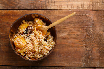 A plate of couscous with saffron and nuts on a wooden table with a wooden spoon. Save a place.