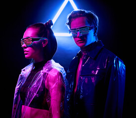 Portrait of confident young people in fashionable cyber outfits standing in dark room with neon triangle sign