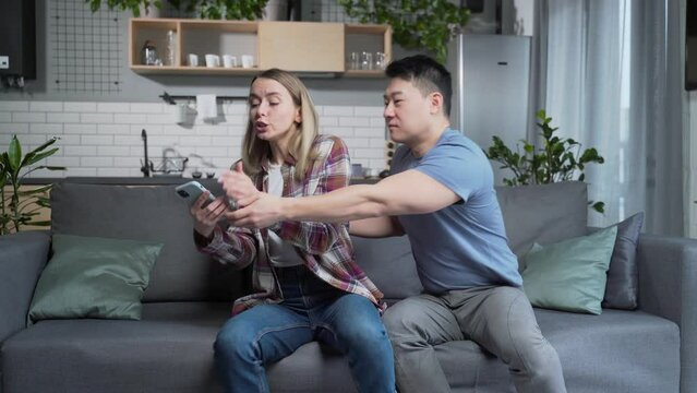 Married couple, man and woman, sitting on the couch at home and arguing over the phone, jealousy. Young family Marital infidelity, Adultery, secret correspondence mistrust of partners and quarrels