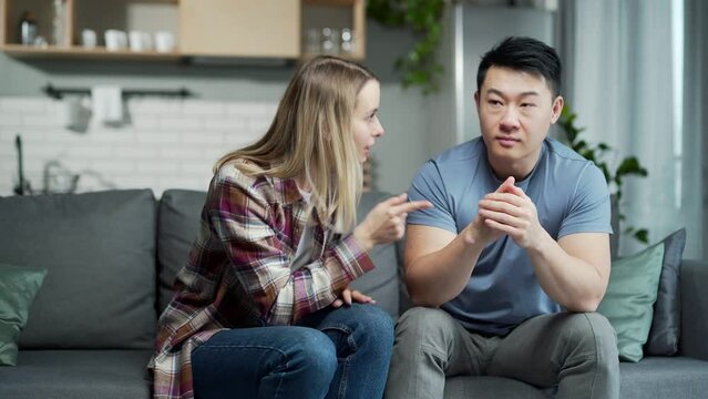 domestic violence woman quarreling with husband. Nervous asian man sitting on the couch in foreground while his wife shouting at him. couple problems and conflict in young family at home