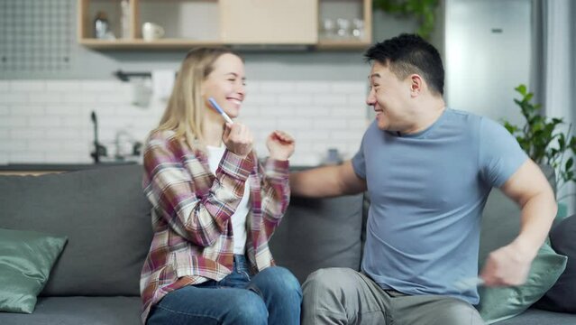 Young family enjoys a positive pregnancy test a happy married couple asian man and woman sit on the couch hug and embracing. Future parents finding out result, expressing excitement. looking good news