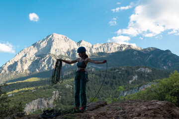 A woman in a helmet coils a rope against the background of a large mountain