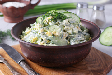Salad with cucumbers, boiled egg, chives and herbs in brown bowl on wooden board