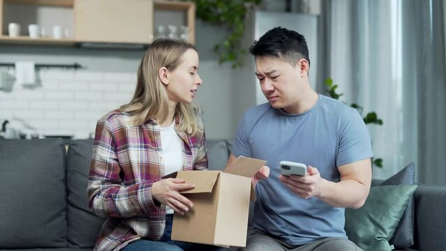 shocked frustrated couple customer open cardboard box receive wrong or damaged shopping order parcel. Sad young asian man and woman unpacking wrong parcel, delivery mistake Upset mad asia people
