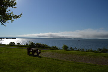 Fototapeta premium A park bench overlooks Lake Superior on a sunny afternoon with blue skies above lake fog near Ashland Wisconsin.