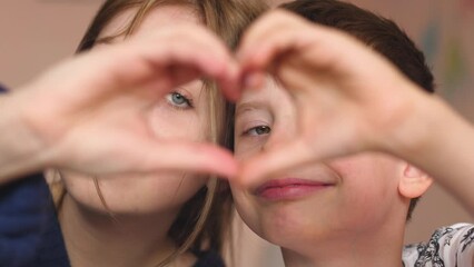 Portrait of a caucasian boy 7-8 years old with his sister 18 years old looking at the camera showing a gesture in the shape of a heart with his hands. Family relationship of brother and sister adult.