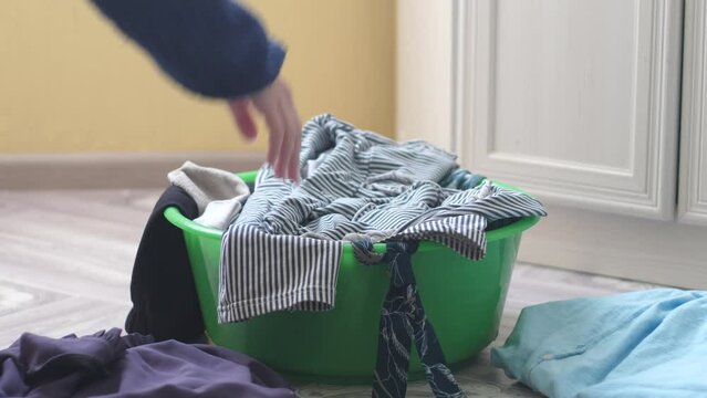 A woman's hand is rummaging through dirty linen. A woman sorts laundry for washing separates dark and light clothes. Home laundry. Housewife getting ready for laundry