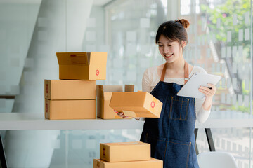 A beautiful Asian business owner opens an online store, she is checking orders from customers, sending goods through a courier company, concept of a woman opening an online business.