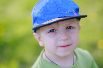 Portrait of a 5-year-old boy in a baseball cap. Happy child on the background of grass with flowering dandelions in a clearing in the city