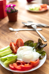vegetables cucumbers, tomatoes, lettuce and poached eggs on a white plate on a wooden oak table. Concept on the theme of healthy eating