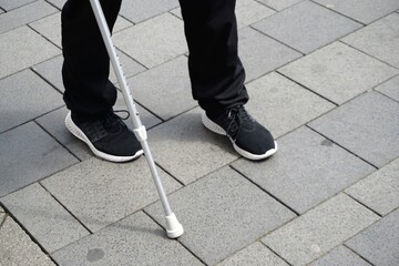 Mann mit schwarzen Turnschuhen und schwarzer Hose mit silbernem Gehstock aus Metall auf Stra&szlig;e 