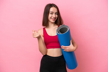 Young sport Ukrainian woman going to yoga classes while holding a mat isolated on pink background...