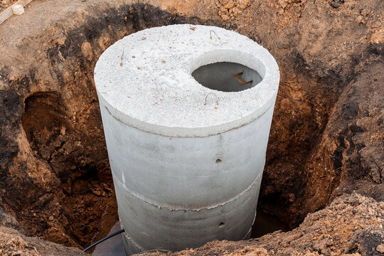 A well made of concrete, a pit for sewerage, a construction site, a connection of communications to the house, the gray color of cement, a round sewer hatch.