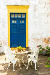 Fototapeta na wymiar White table and chairs in front of colorful doorstep of old traditional house in Brazil