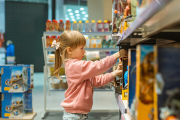 Fototapeta premium Little caucasian girl choosing a new toy in the big baby store. Big shelfs full of toys